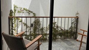 Un balcón con vistas a un edificio, una silla de madera y una mesita.