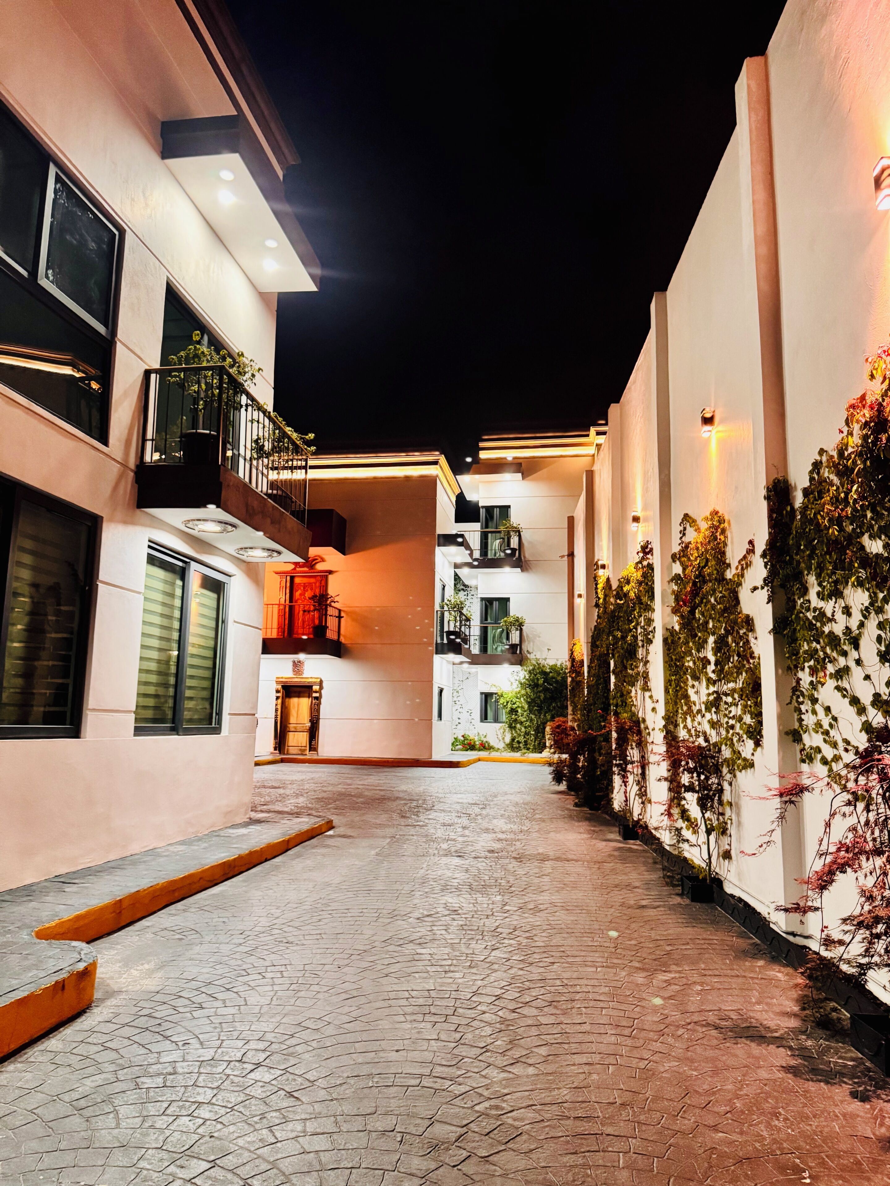 Vista nocturna de un edificio con un patio empedrado, balcones y plantas en macetas.