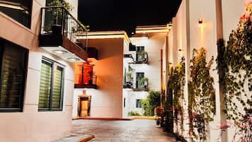 Vista nocturna de un edificio con un patio empedrado, balcones y plantas en macetas.
