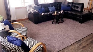 A living room with a black leather sofa, two armchairs, a coffee table, and a rug.