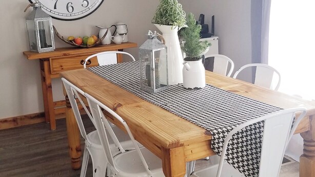 A dining area with a wooden table, white chairs, a large wall clock, and a potted plant.