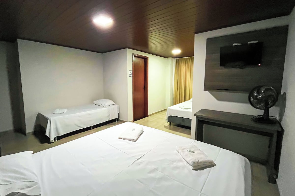 A hotel room with two single beds, a desk, a chair, a TV, and a ceiling fan.