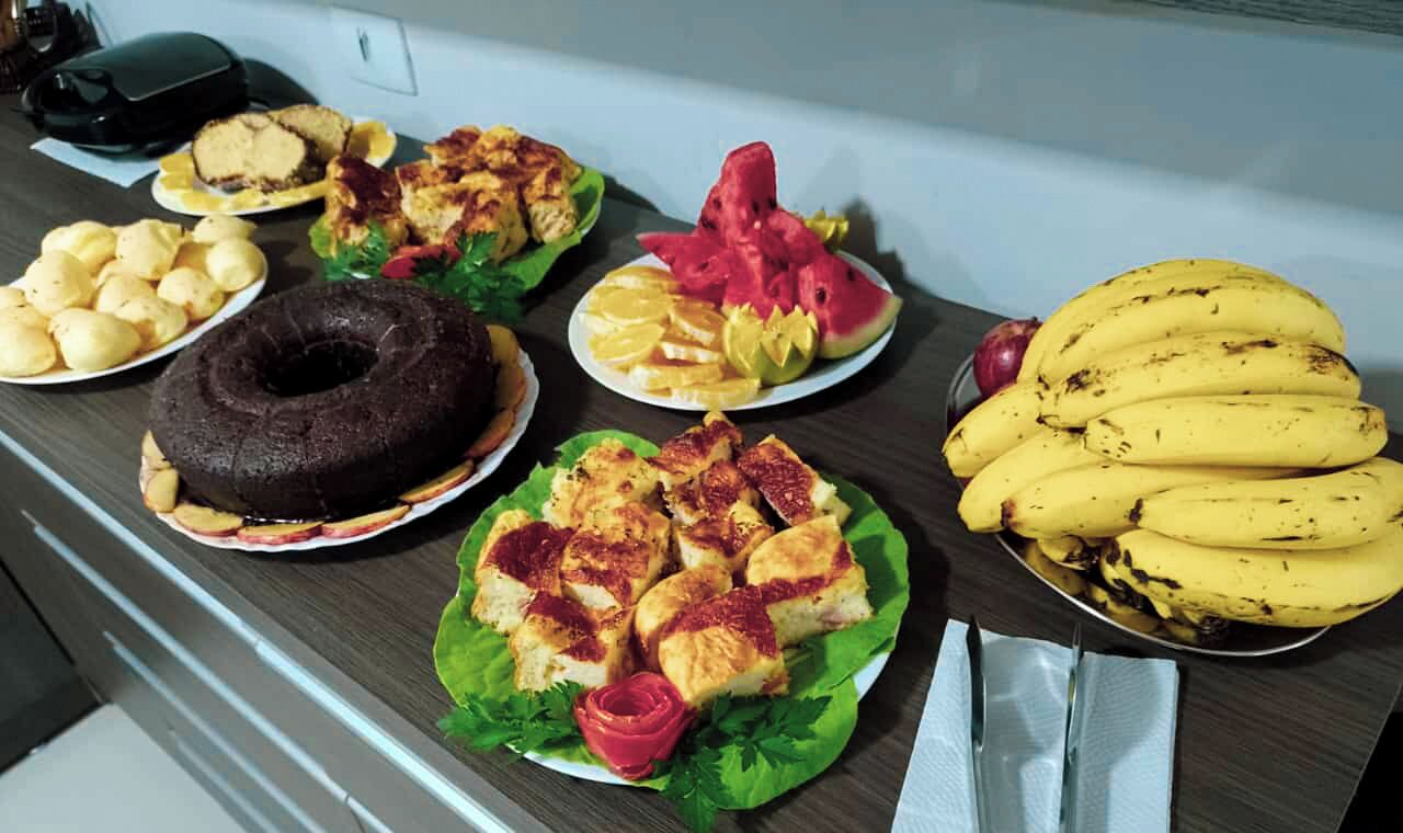 Uma mesa com diversos alimentos, incluindo um bolo de chocolate, fatias de fruta e bananas.