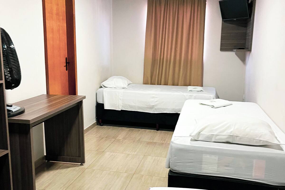 A small, well-lit room with two beds, a desk, and a fan.