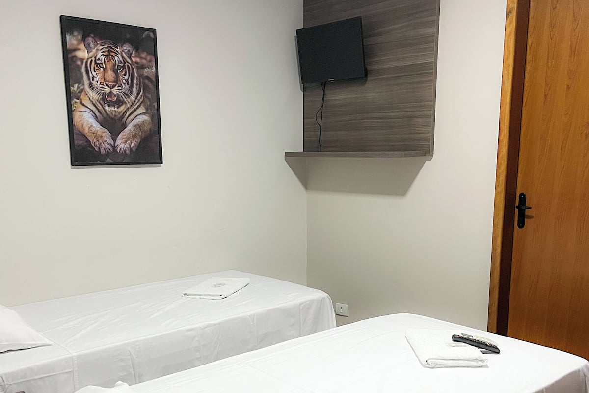 A hotel room with two single beds, a mounted TV, and a wooden door.