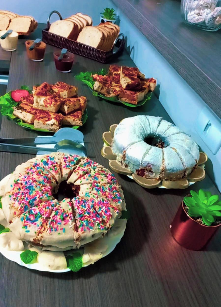 A buffet table with various food items including a large donut with sprinkles, a bundt cake, and several types of bread and pastries.