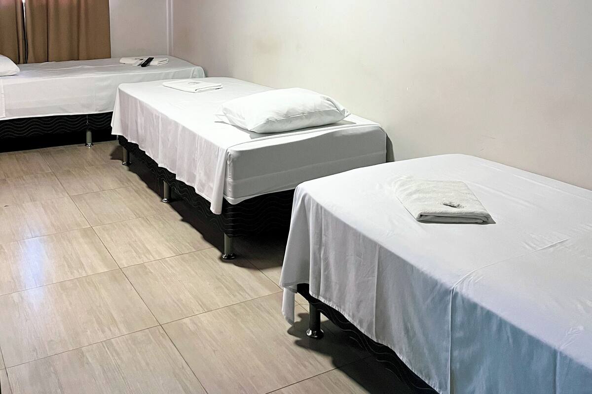 A hotel room with three single beds, a flat-screen TV mounted on the wall, and a wooden floor.