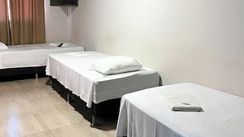 A hotel room with three single beds, a flat-screen TV mounted on the wall, and a wooden floor.