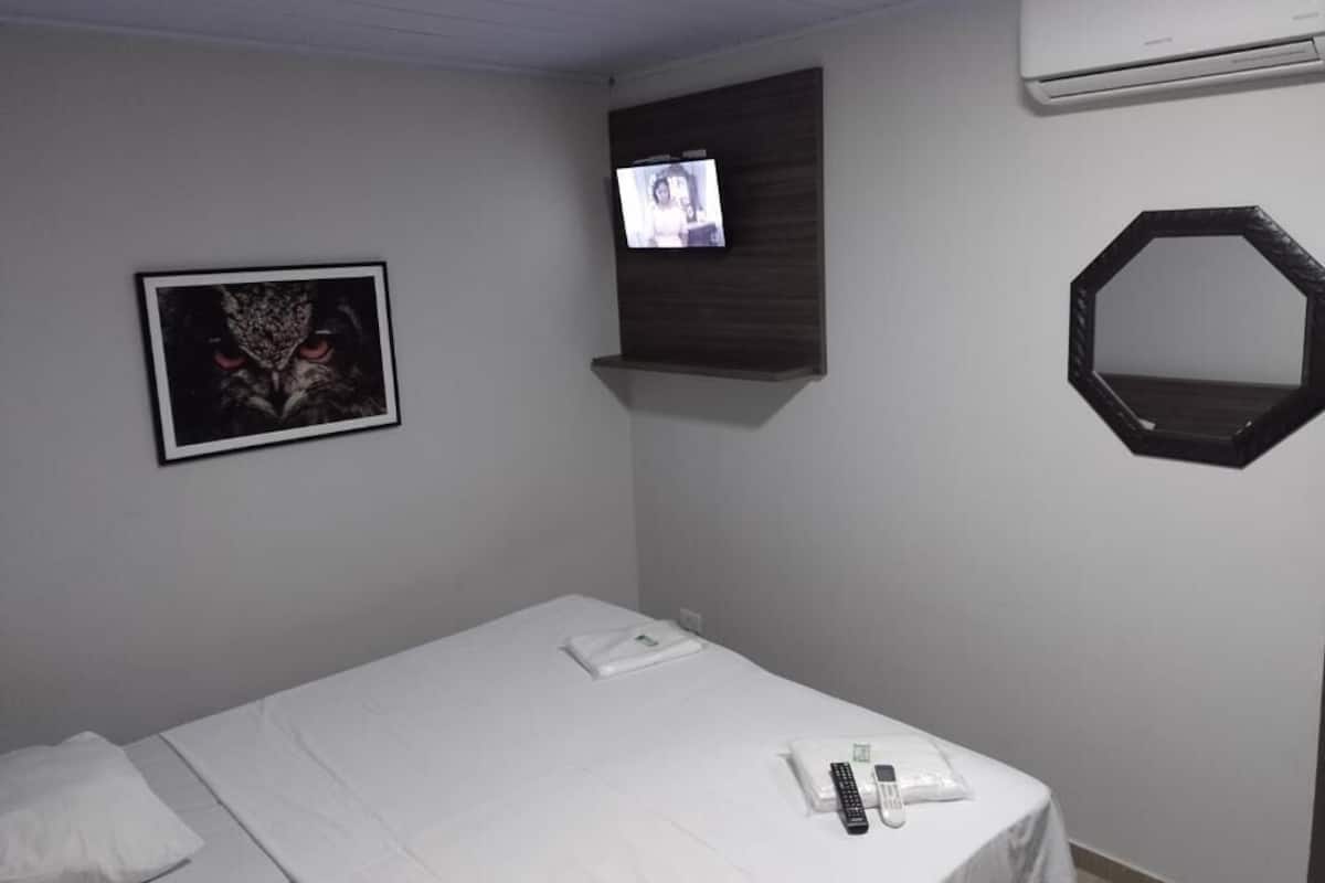 A hotel room with a bed, a mounted TV, a framed picture, and a mirror on the wall.