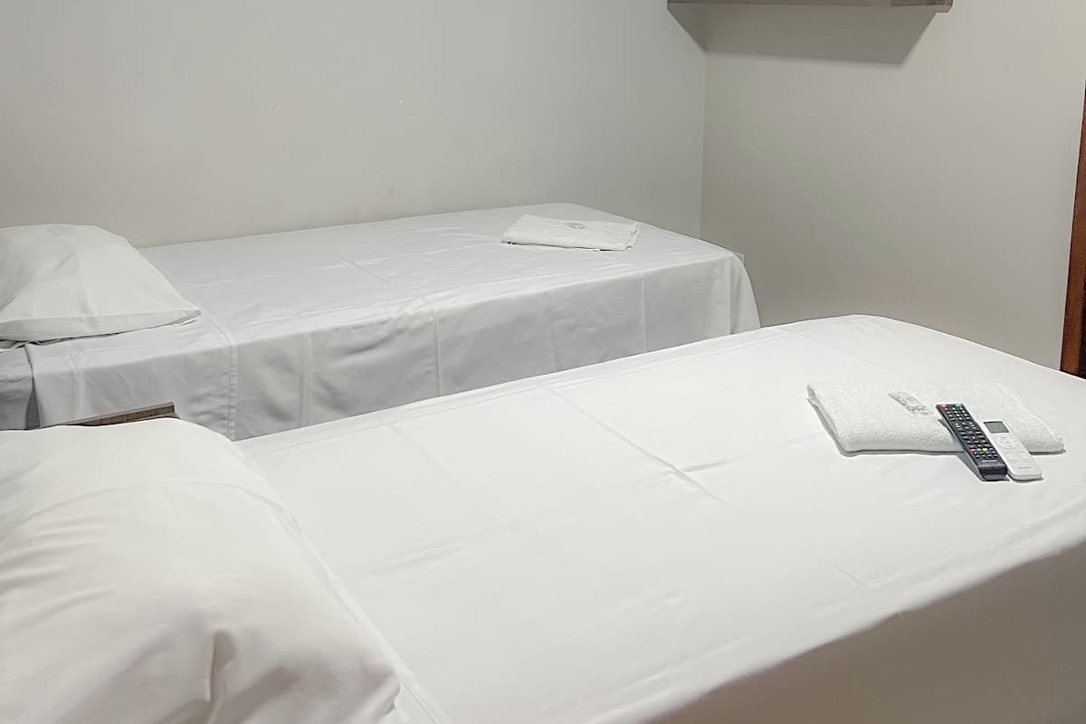 A hotel room with two single beds, a flat-screen TV mounted on the wall, and a remote control on the bed.