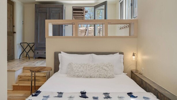 A bedroom with a bed, a nightstand, a lamp, a window, and a staircase.