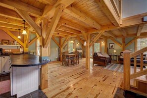 A spacious loft-style room with exposed wooden beams, a kitchen area, and a dining space.
