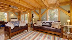 Un intérieur de chalet chaleureux avec un plafond en bois, deux canapés, un tapis à rayures et un panneau indiquant « PLAGE ».