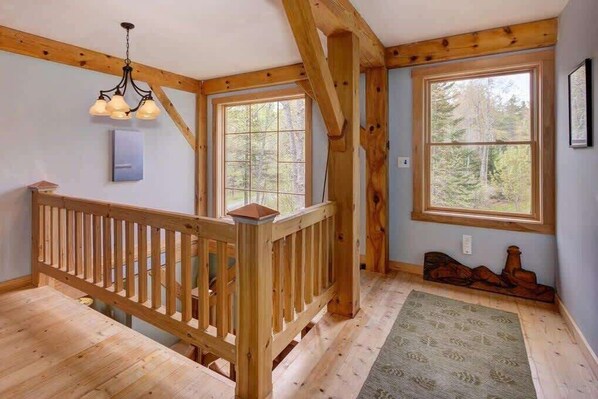 A wooden interior with a staircase, large windows, and a chandelier.