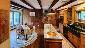 Une cuisine avec des meubles en bois, un îlot central doté d’un évier et un coin repas avec une table et des chaises.
