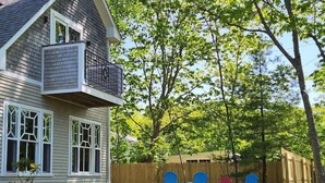 Une maison avec un balcon, une cour arrière clôturée et plusieurs chaises Adirondack.