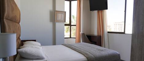 A hotel room with a bed, a desk, a TV, and a window with curtains.