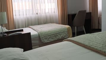 A hotel room with two beds, a desk, a chair, and a window with curtains.