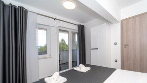 Une chambre d’hôtel moderne avec un grand lit, une porte-fenêtre coulissante donnant sur un balcon et une porte en bois.