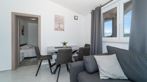 Un salon moderne avec un canapé gris, une table à manger avec des chaises, une petite plante et une fenêtre avec des rideaux.