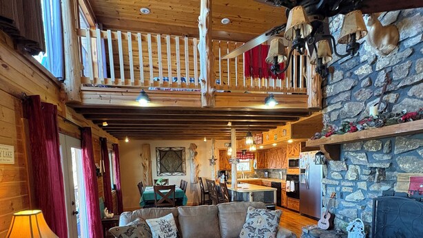 Interior acogedor de una cabaña con techo de madera, chimenea de piedra, comedor y sala de estar con sofá y mesa de centro.