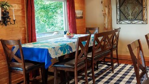Un interior de madera con piso a cuadros, una mesa cubierta con mantel floral y sillas de madera.