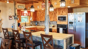 Una cocina rústica con vigas de madera, una isla central con taburetes de bar, un refrigerador y un microondas.
