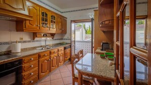 A kitchen with wooden cabinets, a granite countertop, and a dining area with a table and chairs. - Holiday Home 'Vez' with Mountain View, Private Garden and Wi-Fi (Arcos de Valdevez)