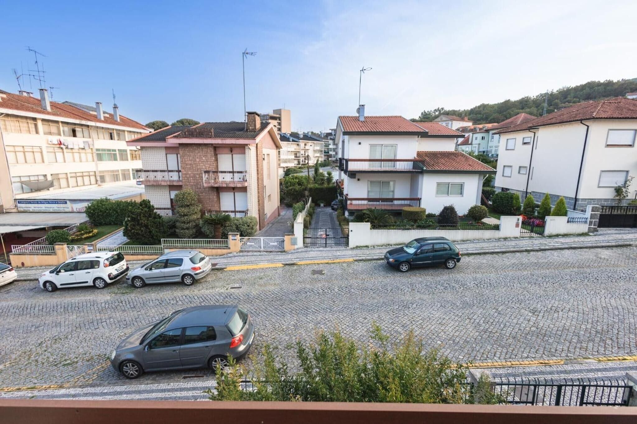 A residential street with parked cars, houses, and a building with a sign.