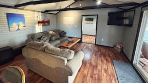A cozy living room with a sofa, wooden flooring, and artwork on the walls. - Ultimate Private Lake Hideaway with Hot Tub (Lac La Hache)