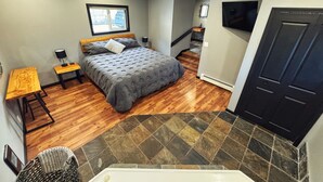 A bedroom with a bed, a desk, a chair, a TV, and a bathroom with a bathtub. - Ultimate Private Lake Hideaway with Hot Tub (Lac La Hache)