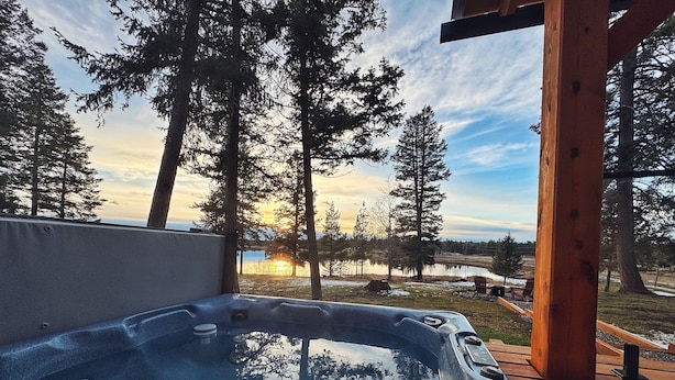 A hot tub on a wooden deck with a view of trees and a sunset. - Ultimate Private Lake Hideaway with Hot Tub (Lac La Hache)