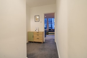 Un couloir étroit avec une moquette de couleur claire, un meuble en bois doté de tiroirs et un tableau encadré accroché au mur.