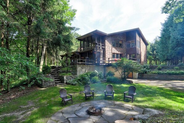 Eine zweistöckige Lodge mit Kamin aus Stein, Sitzgelegenheiten im Freien und einer Steintreppe, die zu einer Terrasse führt.