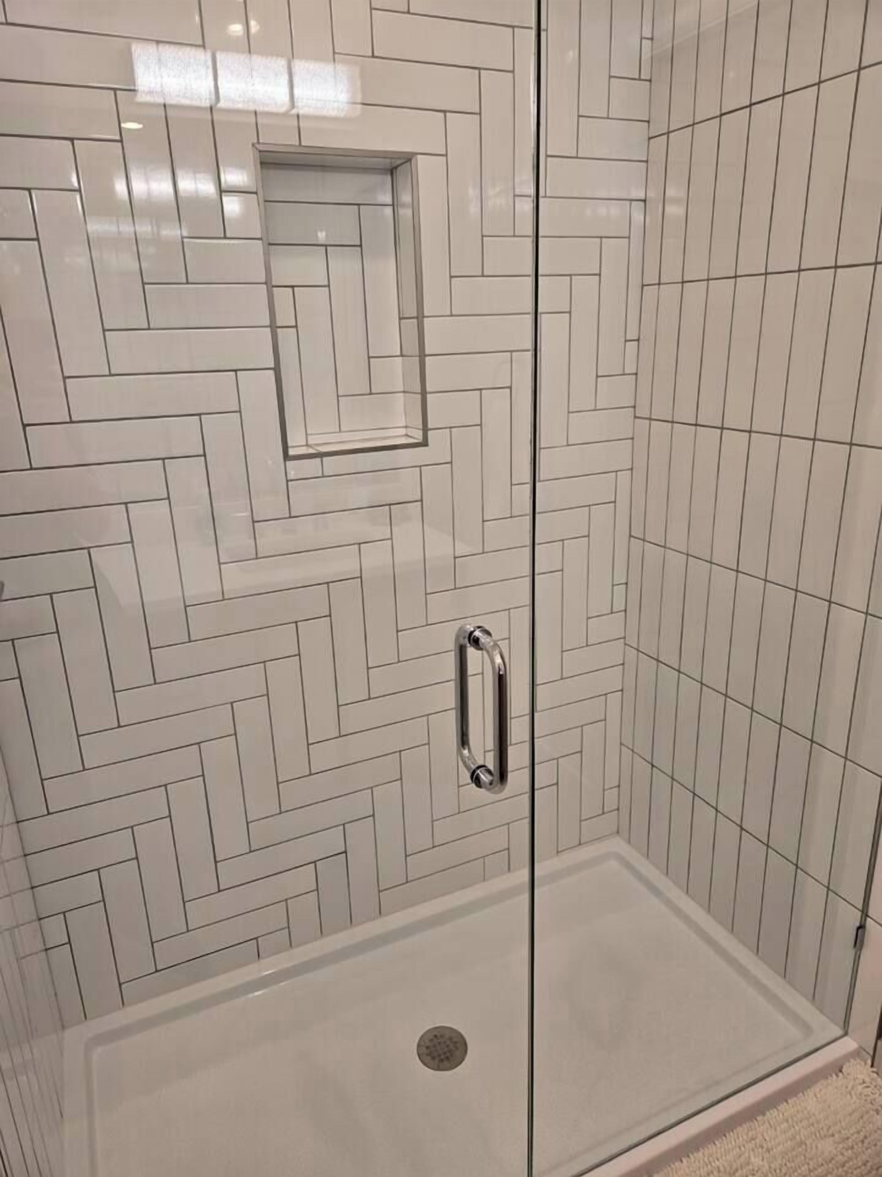 A shower with a herringbone tile pattern and a glass door with a handle.