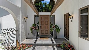 A covered entrance with a brown door, two potted plants, and a stone pathway leading to the door. - Private Pool 5 Minutes From Lake Michigan (South Haven)