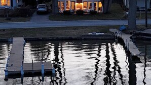 A house with a dock extending into a calm body of water, surrounded by trees and a grassy area. - Hutchins Lake Retreat (Fennville)