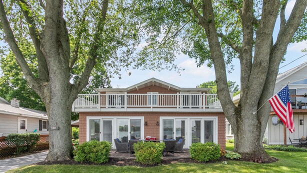 A two-story house with a balcony, a patio with outdoor furniture, and an American flag. - Hutchins Lake Retreat (Fennville)