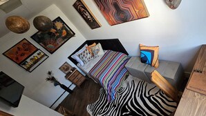 Un dormitorio con una cama, un tapete estampado con motivos de cebra, un aparador de madera y varias obras de arte en las paredes.