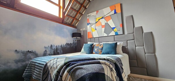 A bedroom with a bed, a mural of a forest, a modern abstract painting, and a skylight.