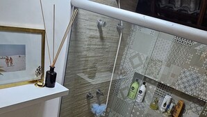 Un baño con inodoro, ducha con puerta de cristal, lavabo con espejo y repisas con artículos de aseo.