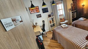 Habitación de hotel con dos camas, un escritorio, una silla, una estantería y una ventana con cortinas.
