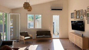 Un salon spacieux avec une grande fenêtre, un canapé, un fauteuil, un téléviseur et un meuble en bois.