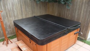 A hot tub with a wooden exterior and a black cover, featuring a wooden bench and a small step for access. - Modern 7BR Family Oasis in Salt Lake Valley (Sandy)