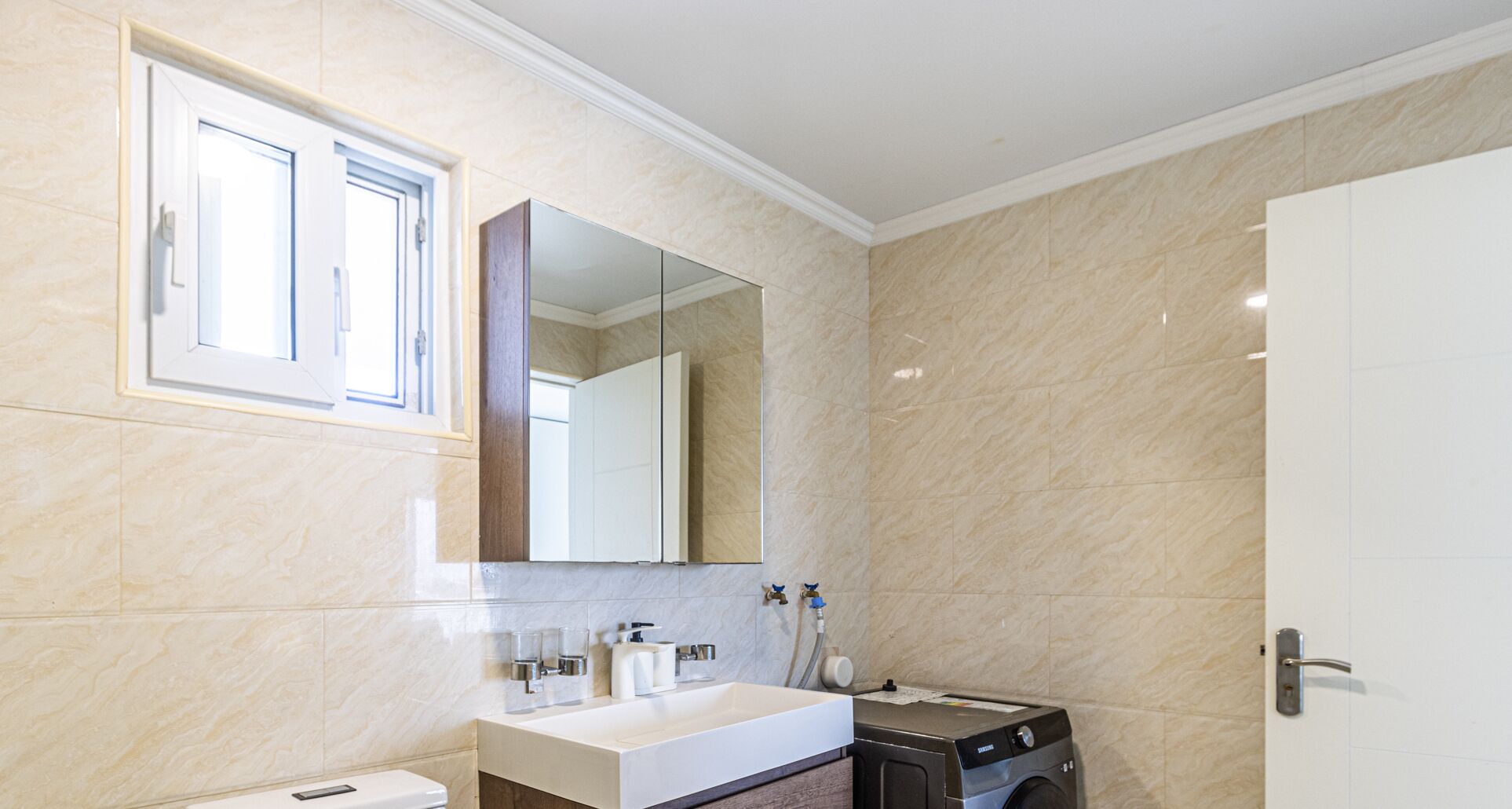 A modern bathroom with a large mirror, a sink, a toilet, and a washing machine.