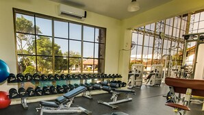 Une salle de sport équipée de matériel d’exercice, dotée d’une grande fenêtre et offrant une vue sur les arbres et les bâtiments.
