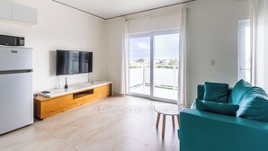Un appartement moderne doté d’une cuisine, d’un téléviseur à écran plat, d’un canapé de couleur turquoise et d’un balcon avec vue.