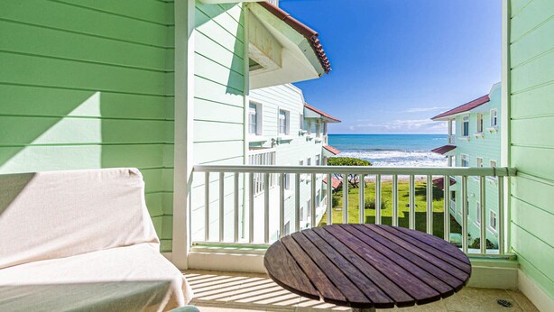 A balcony with a view of the ocean, a wooden table, and a cushioned chair. - Oceanfront Apartment in Cabarete With Pool and Beach Access (Sosúa)