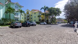 A parking area with several cars, a paved surface, and multi-story buildings with balconies and palm trees. - Oceanfront Apartment in Cabarete With Pool and Beach Access (Sosúa)