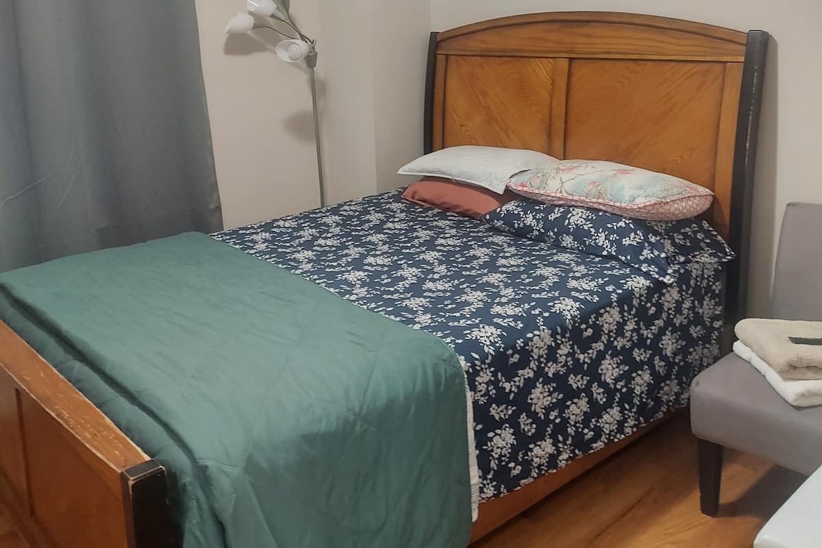 A single bed with a floral bedspread, a wooden headboard, and a green throw blanket.